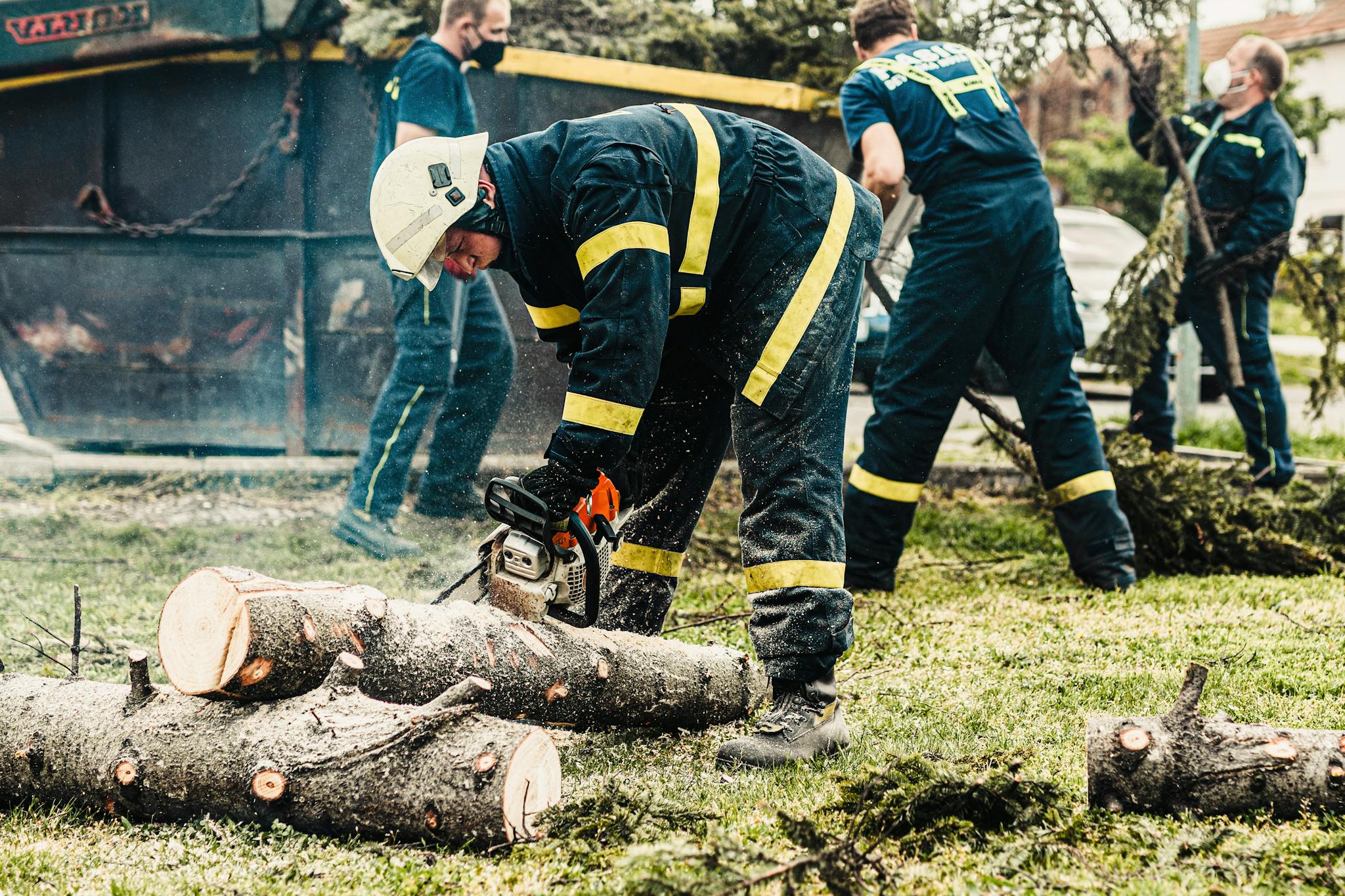 Firefighters in protective gear using a chainsaw to clear fallen trees outdoors. Teamwork in action.